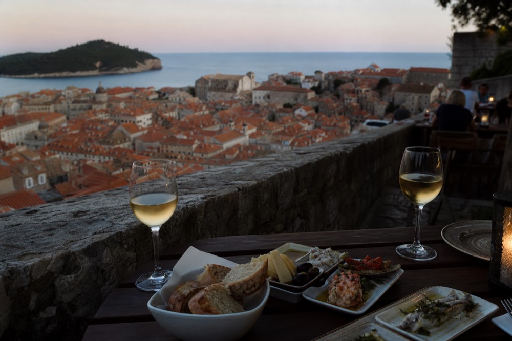 A table set with small tasting plates, bread and glasses of white wine at dusk