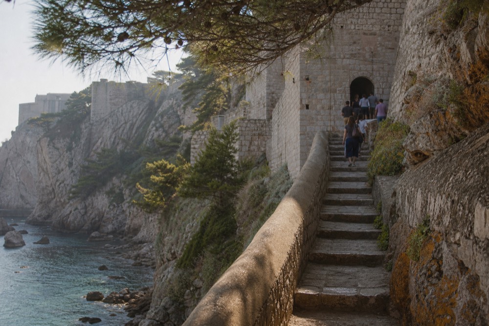 Stone stairway leading up to a fortress gate above a small rocky bay