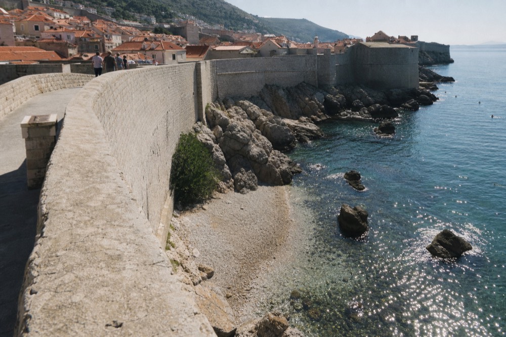 The city walls walkway curving above red rooftops toward the sea