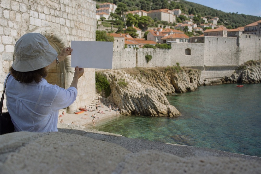 A guide holding up a blank card beside a stone archway, comparing it with the view