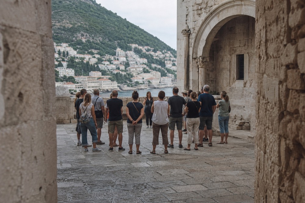 A small walking group in Dubrovnik listening to a guide in a shaded limestone square