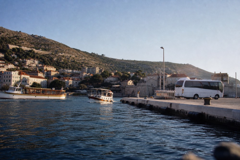 A white shuttle bus parked at a coastal terminal with luggage trolleys nearby