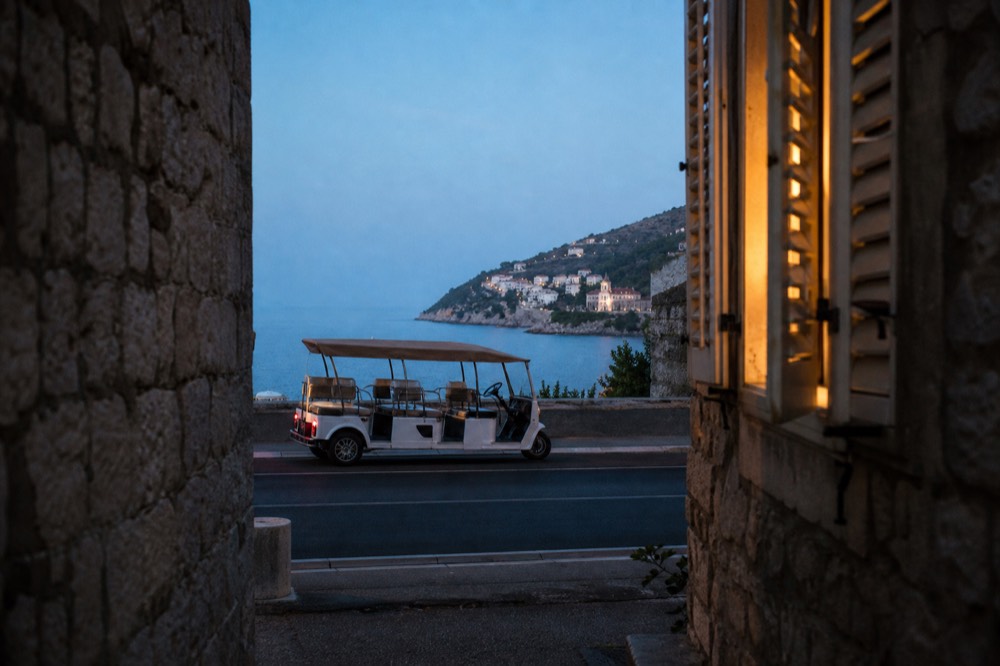 An open-sided electric tuk-tuk vehicle parked on a viewpoint road above the sea