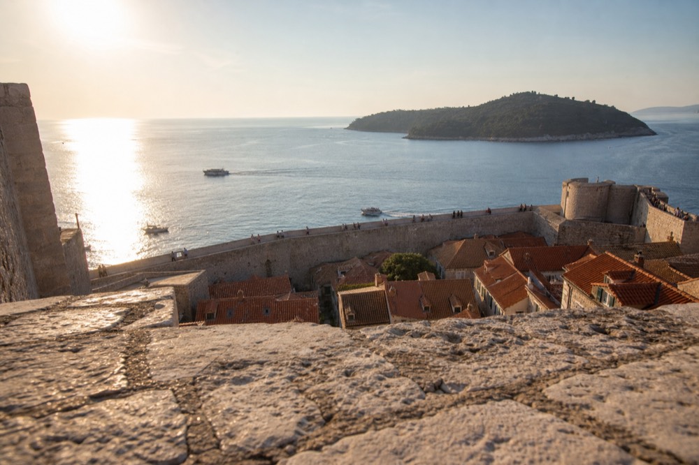 Stone fortification walls rising above red rooftops with the Adriatic sea beyond