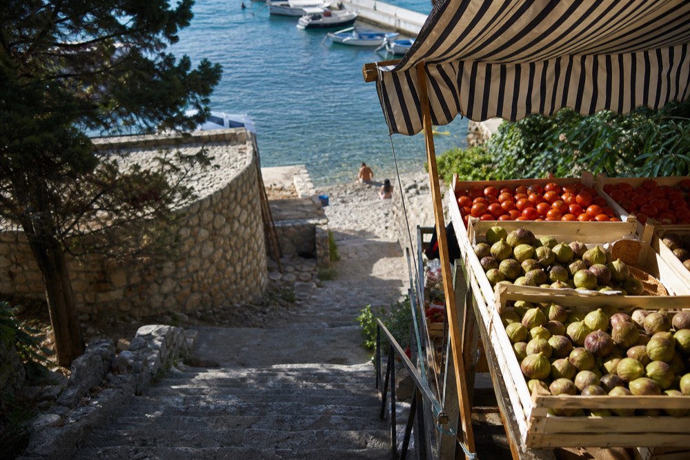 Wooden market crates filled with fresh figs and tomatoes under a striped awning