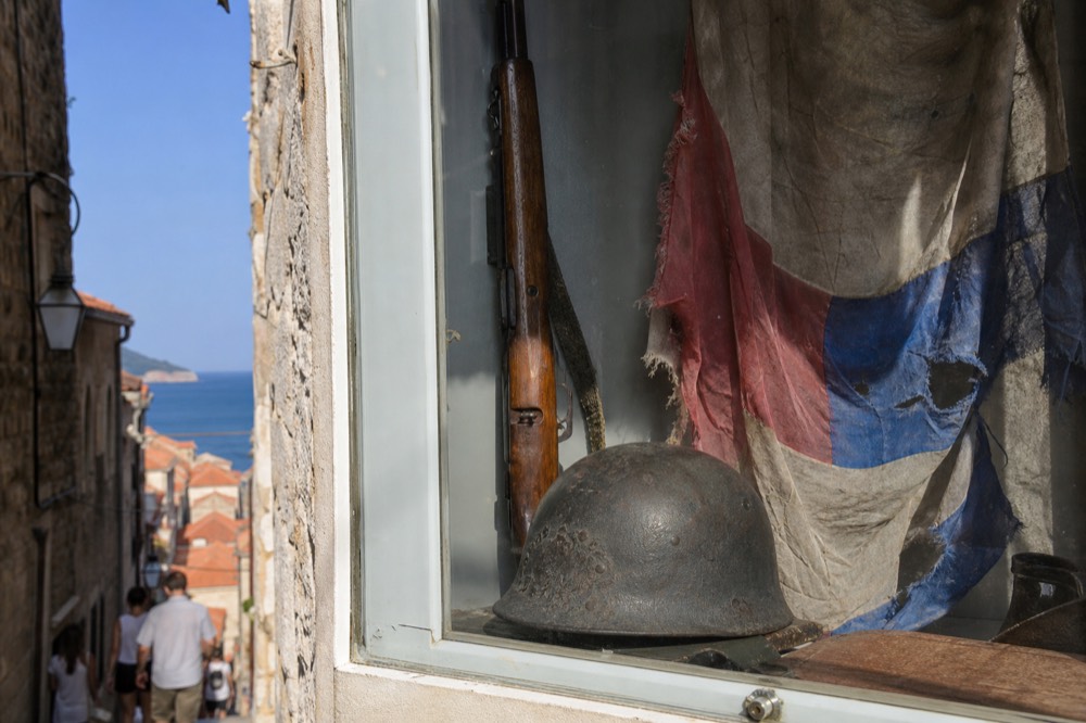 A close-up of a display case containing a soldier's helmet, a rifle, and a tattered Croatian flag.