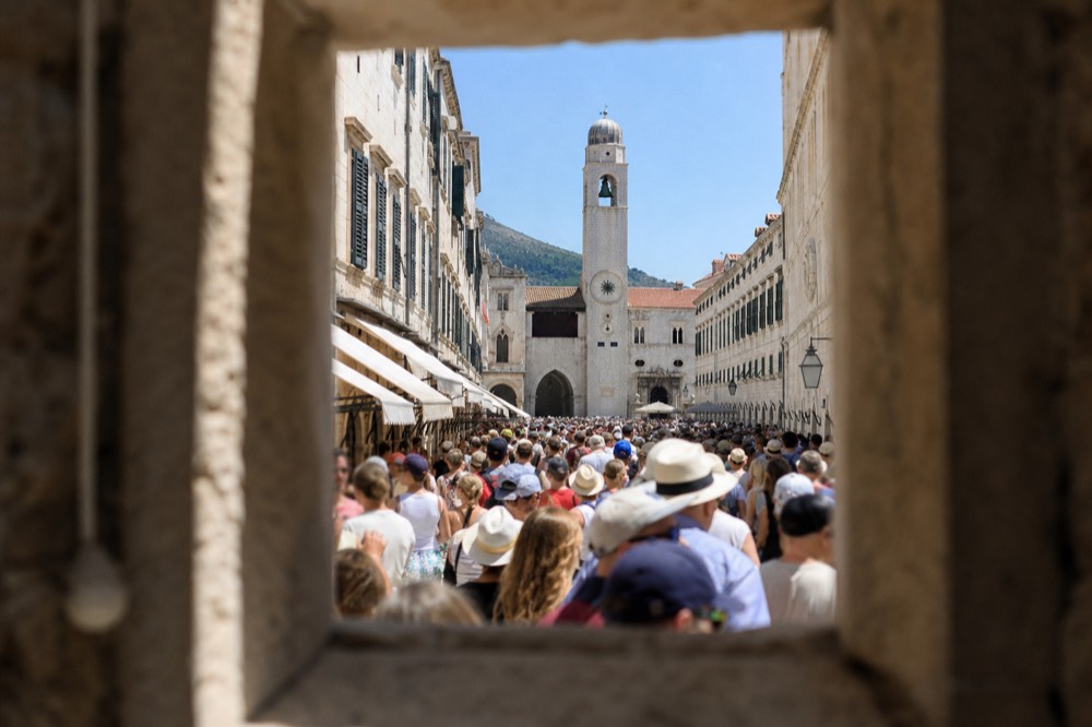 A crowded Stradun in the middle of the day, with tourists packed shoulder to shoulder under the sun.