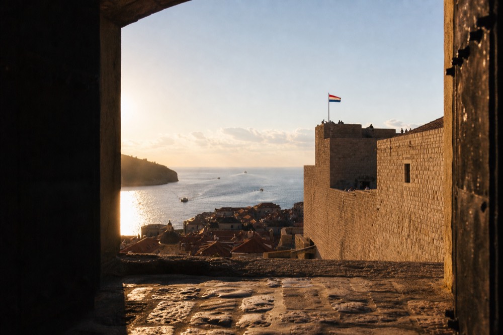 The stone ramparts of Fort Imperial, with a Croatian flag fluttering in the wind and the Old Town visible far below.