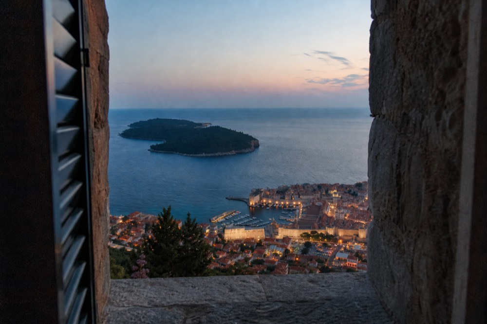 A panoramic view from the fort's ramparts, showing the entire Old Town, the Adriatic Sea, and the island of Lokrum in the distance.