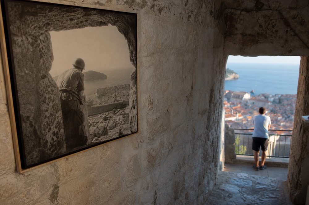 A black-and-white photograph from the museum showing a soldier looking out over the Old Town through a hole in the fort's wall.