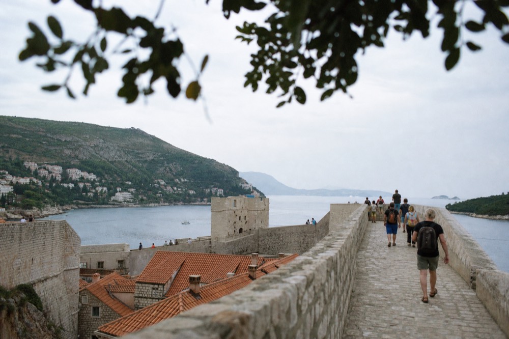 Walkers on the Dubrovnik city walls high above red rooftops and the sea