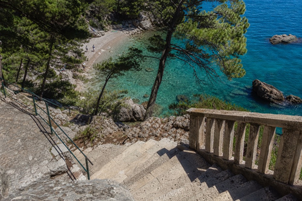 Clear turquoise water washing onto a rocky island beach with pine trees