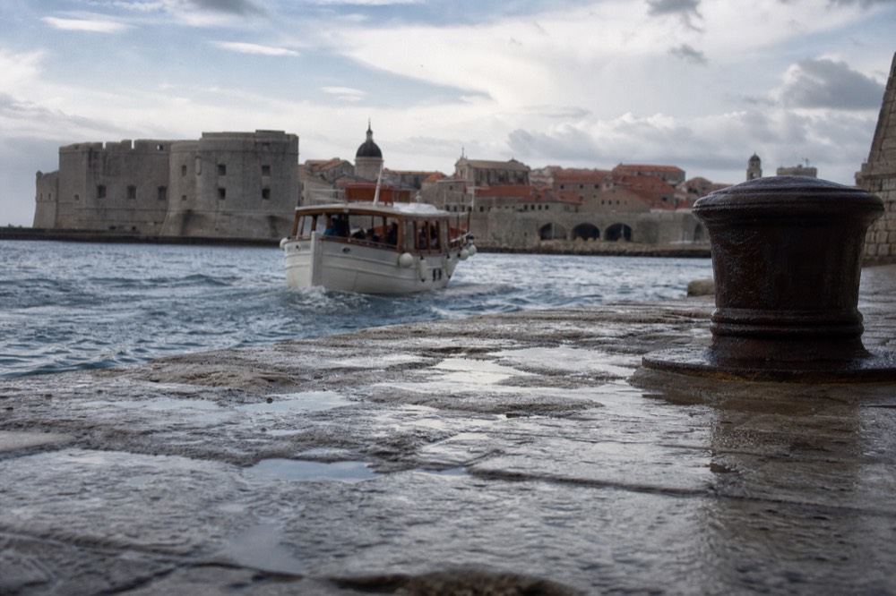 Passenger boat leaving the old city harbour toward open water in morning light
