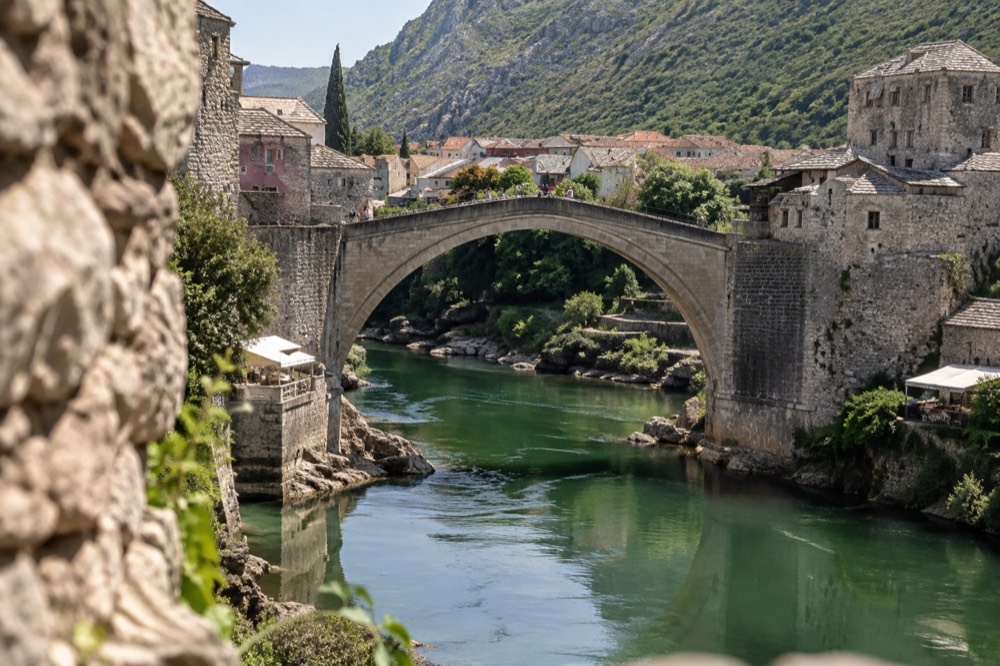 A stone arch bridge spanning a green river with old town buildings on both banks