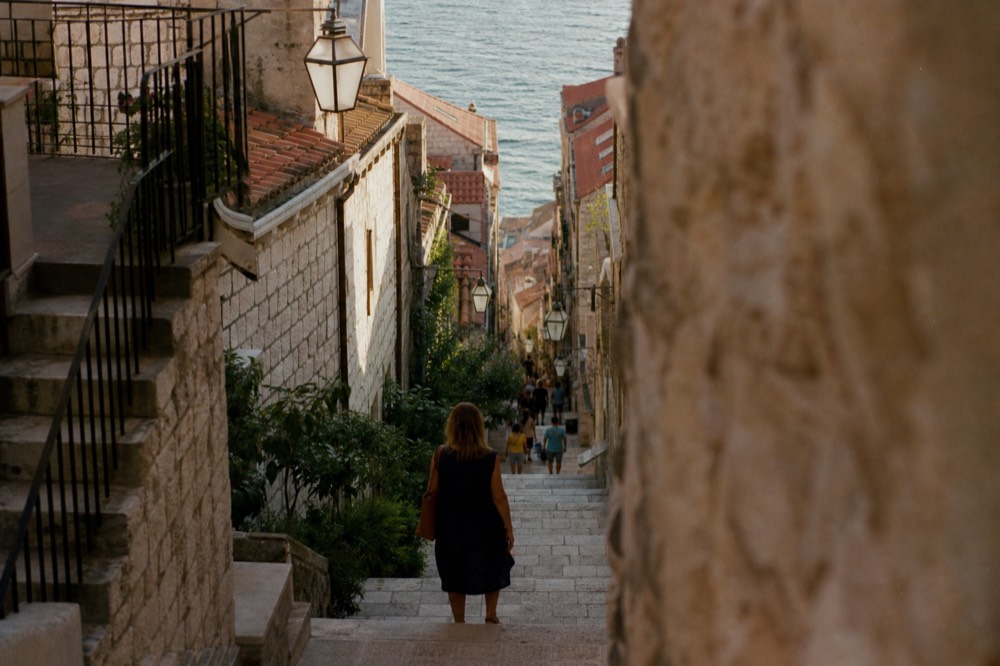 Warmly lit Old Town street in Dubrovnik with people strolling in the evening
