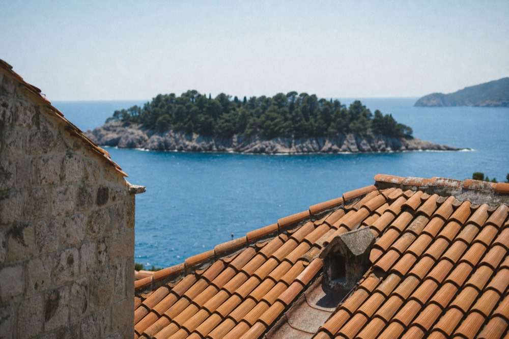 A small island with pine trees rising from calm blue Adriatic water near Dubrovnik
