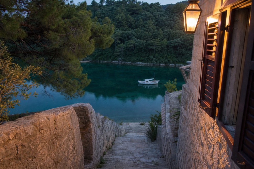 A small boat anchored in a calm green lake surrounded by forest on Mljet