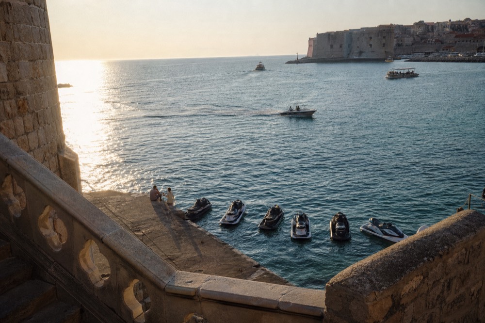 A line of jet skis floating on turquoise water beside a concrete beach slipway