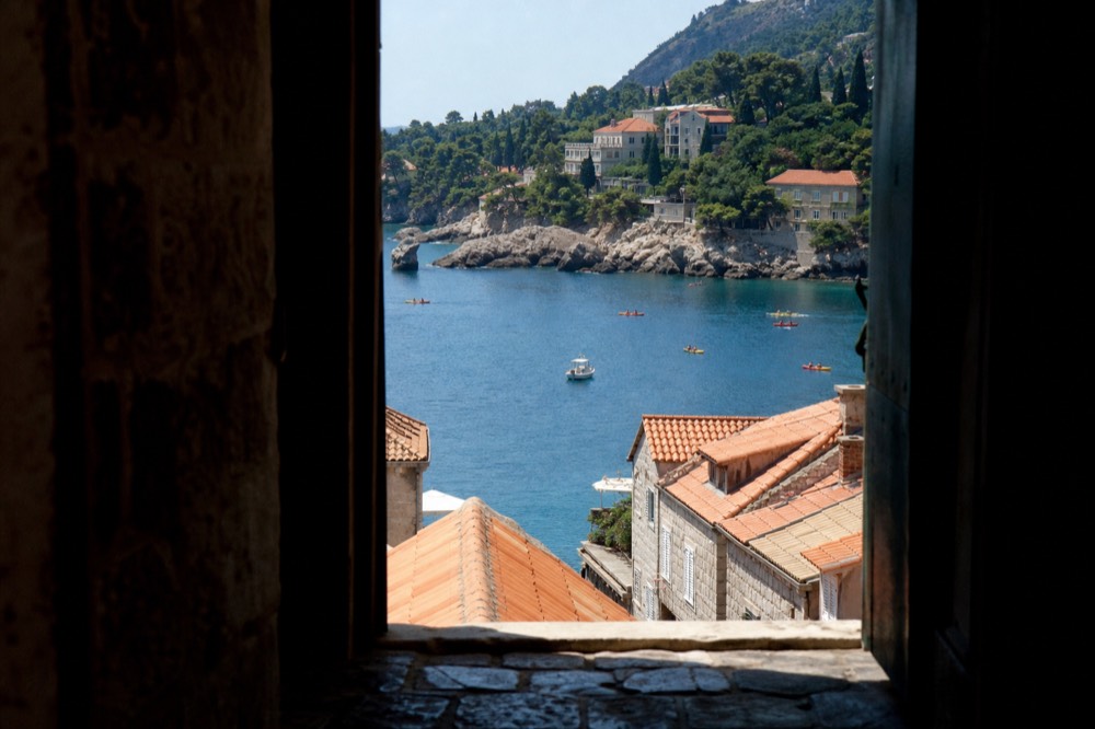 A calm Adriatic bay with kayaks and small boats near a tree-lined shore