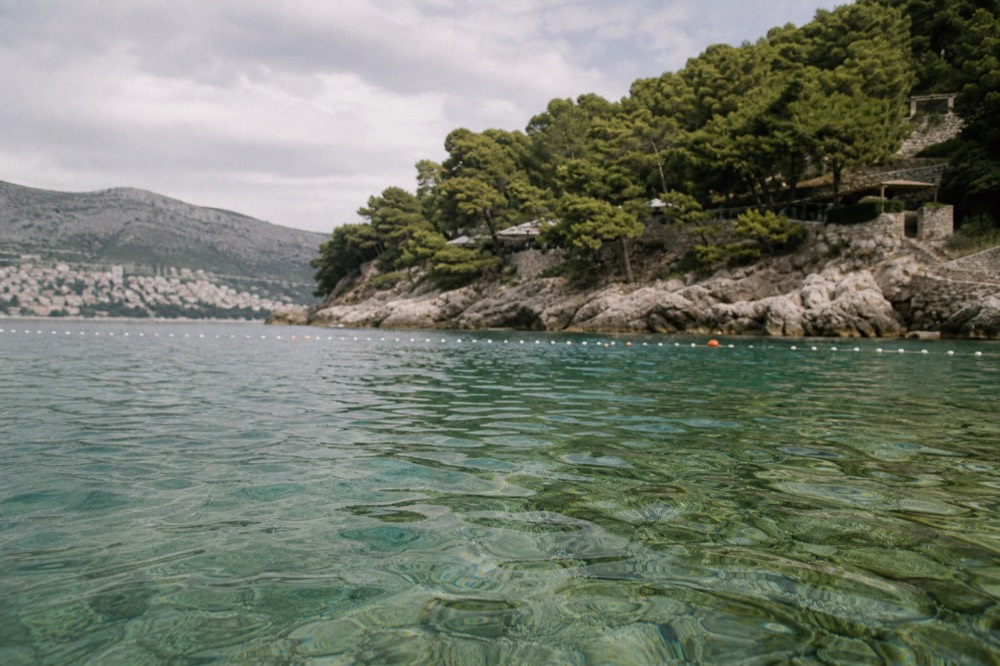 A rocky shoreline with clear shallow water and warning buoys marking a swimming area