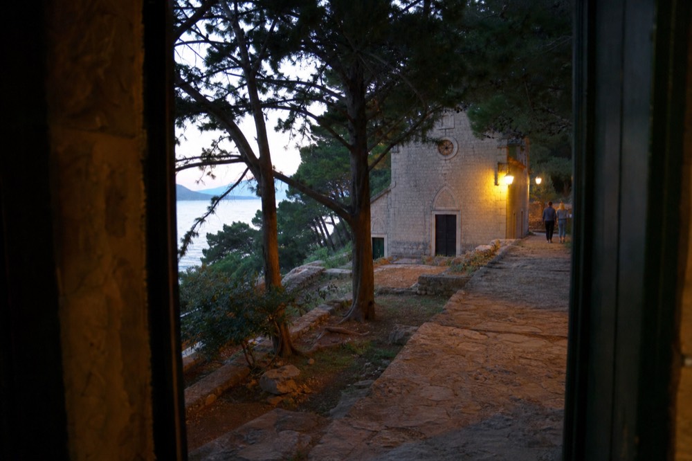 A pine-shaded footpath leading toward a small stone church