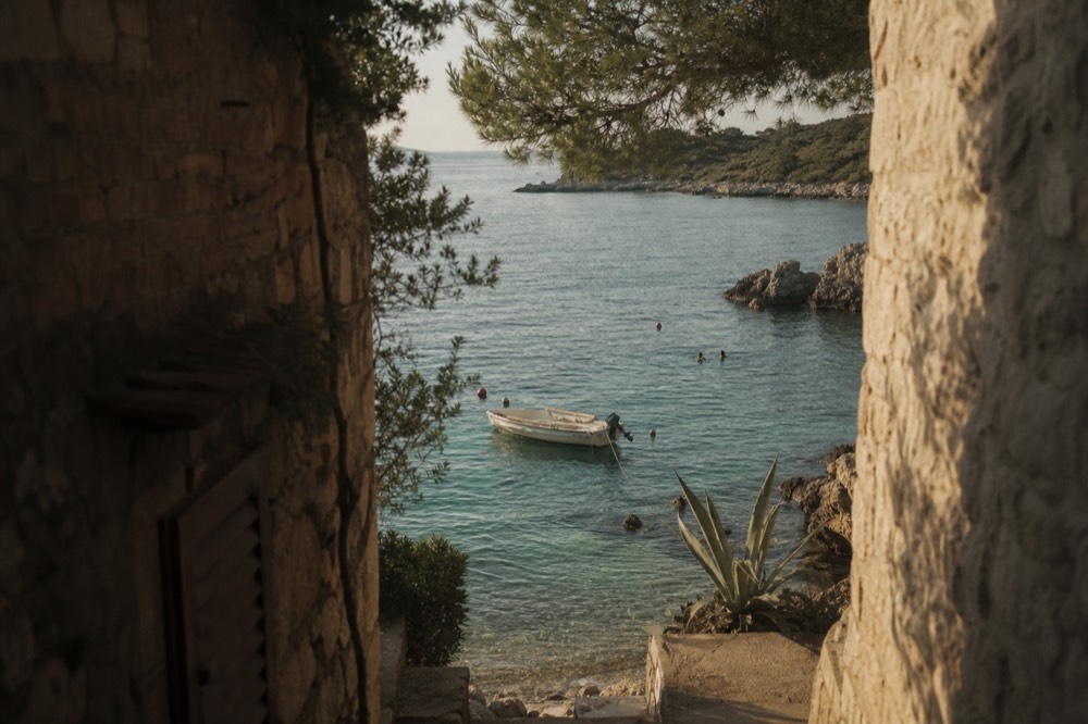 A small open boat anchored in a rocky cove with swimmers nearby