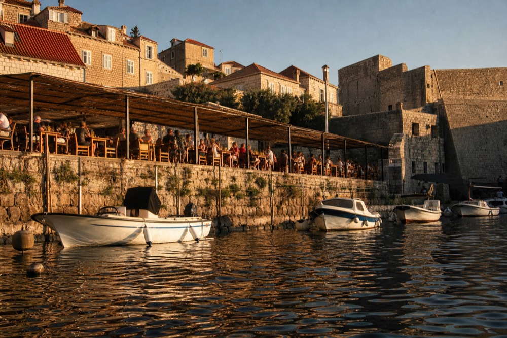 Harbourside terrace with diners at wooden tables beside fishing boats at sunset