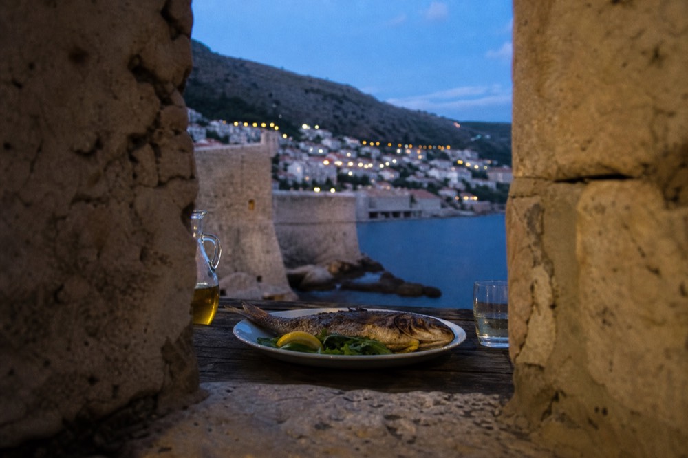 Plated whole grilled fish with lemon, olive oil and greens on a rustic table