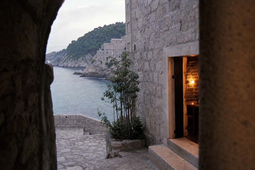 The open door of a stone tavern at dusk, warm light spilling onto the step outside