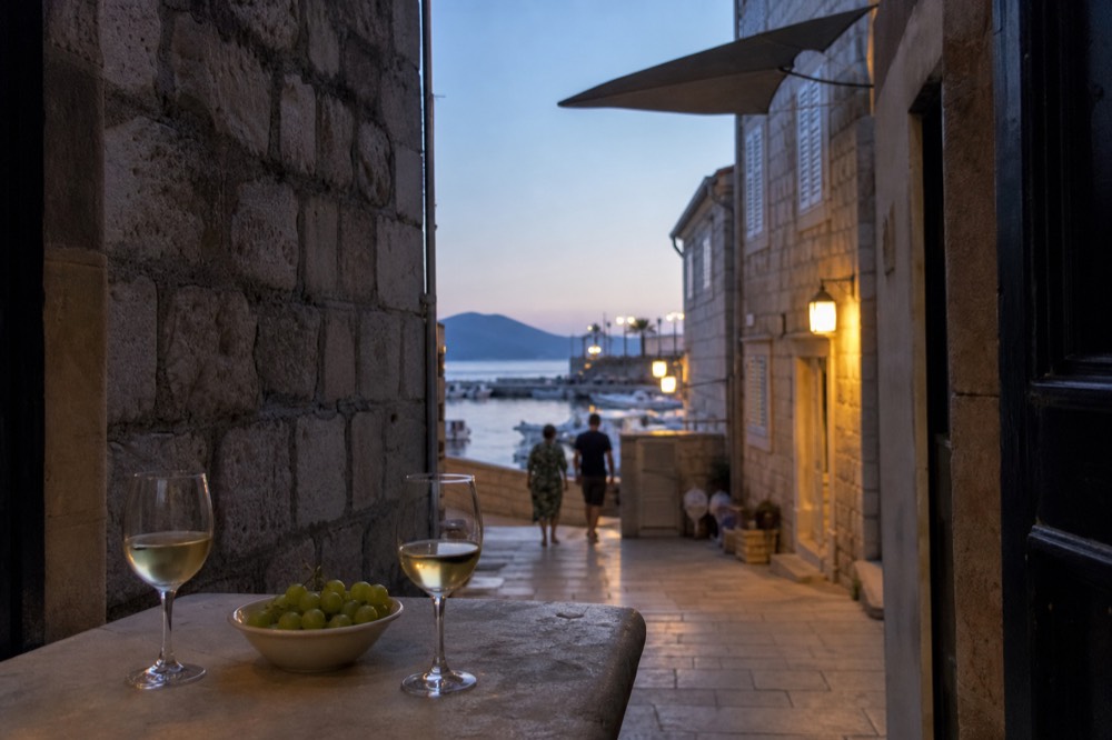 Glasses of white wine on a stone table beside a bowl of green grapes