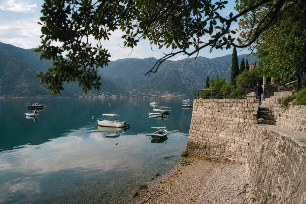 Boats moored on calm water in the Bay of Kotor with mountains reflected in the surface