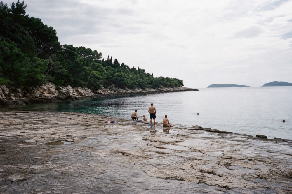 Swimmers on flat rocks beside clear turquoise water at Lokrum