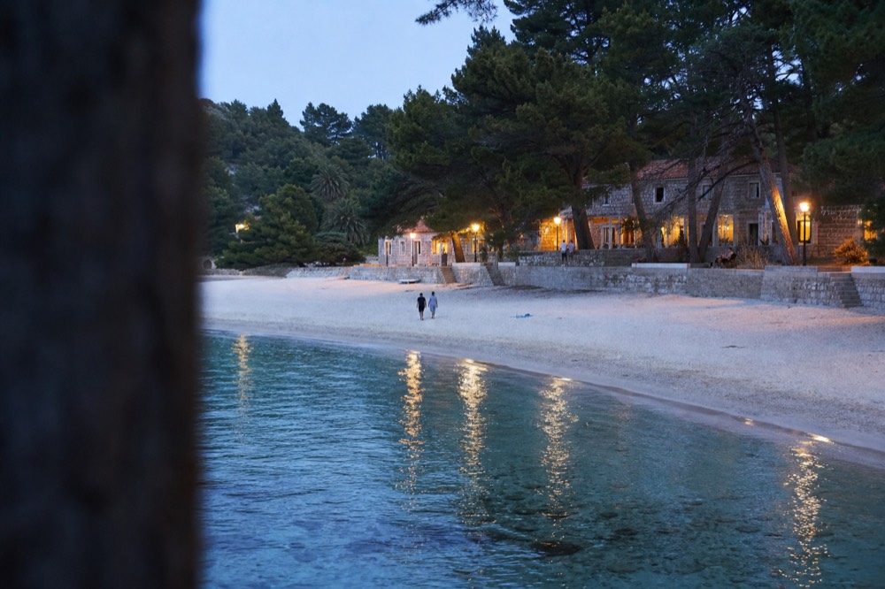 A wide sandy beach in a pine-fringed bay with calm shallow turquoise water