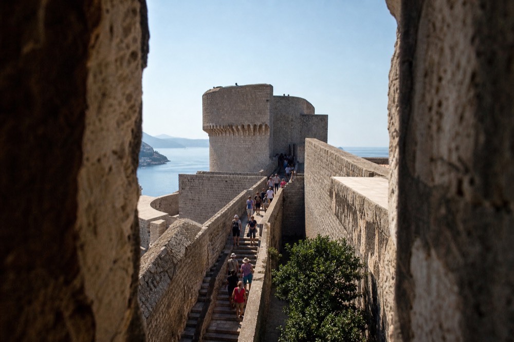 The walls packed with visitors in the morning sun, with the sea in the distance
