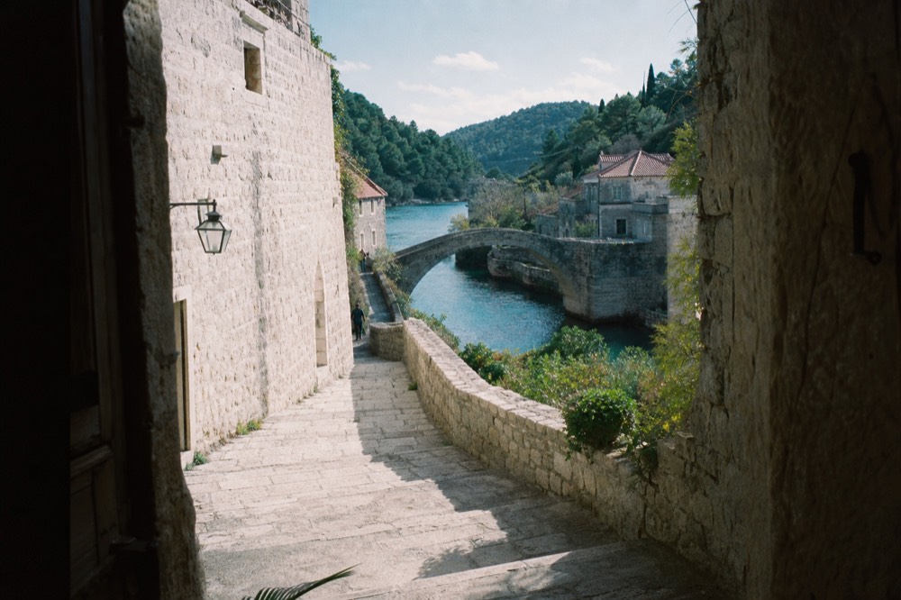 A stone bridge arching over a turquoise river between old riverside buildings