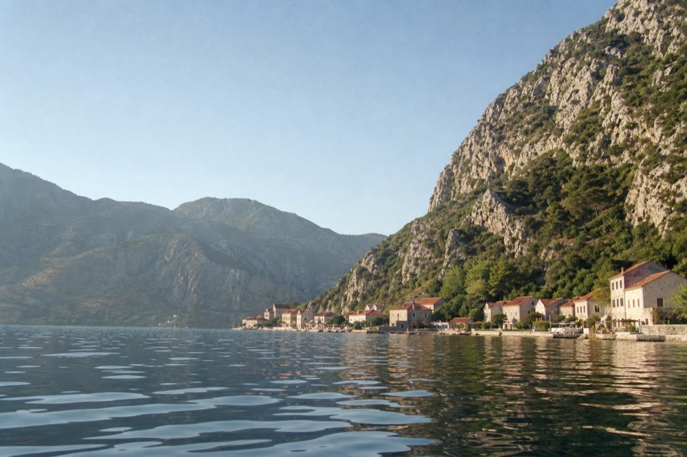 Steep mountains dropping into a calm blue bay with a small town at the shoreline