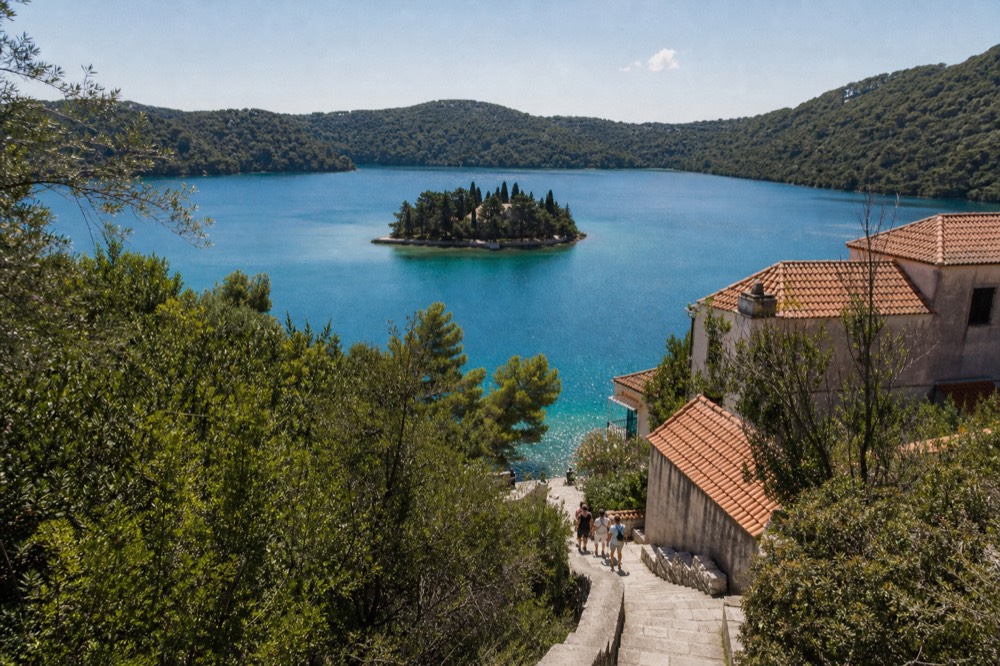 A clear turquoise salt lake surrounded by pine forest with a small islet in the middle