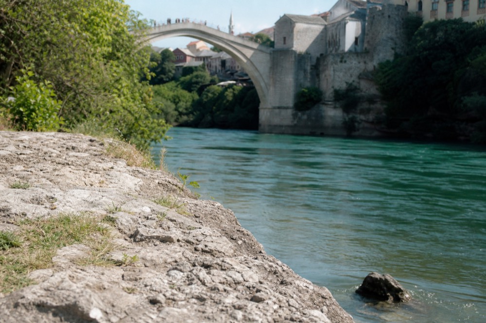 The arched old bridge of Mostar above a turquoise river with old stone buildings on both banks