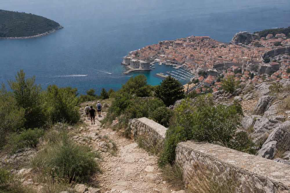 A rocky walking path descending the slope of Mount Srd with Dubrovnik Old Town and the sea in the distance
