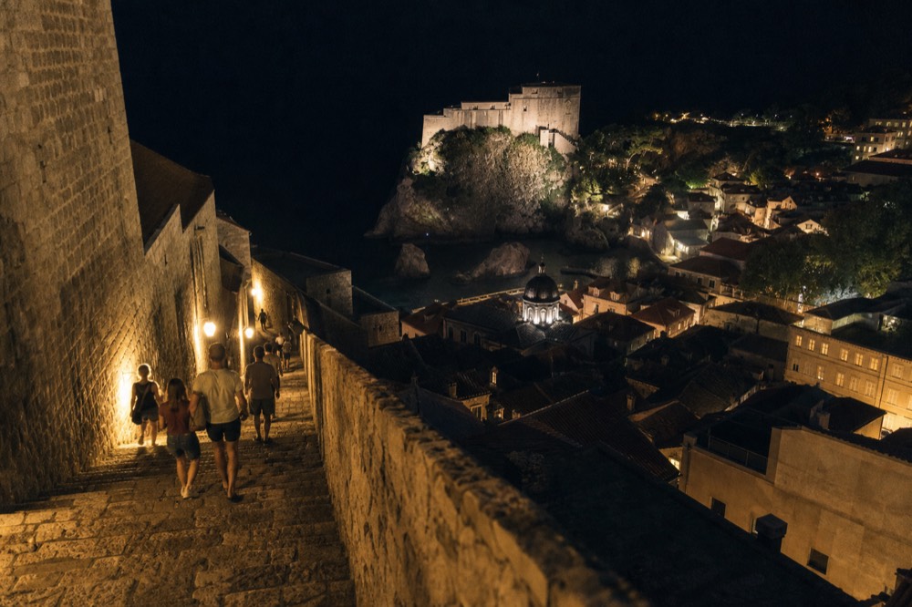 A floodlit stone fortress above city rooftops at night in Dubrovnik