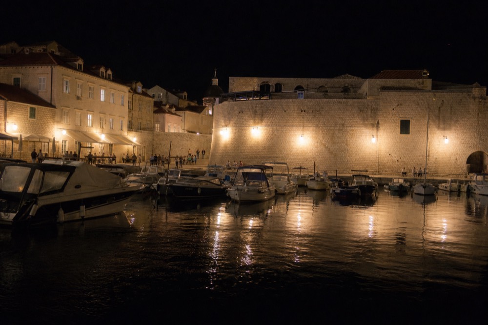 A harbour at night with moored boats reflected in calm dark water under street lamps