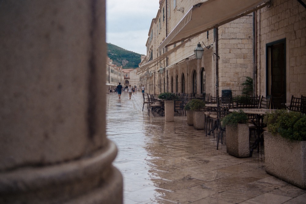 A wide polished limestone street in an old town lined with stone buildings and cafe tables