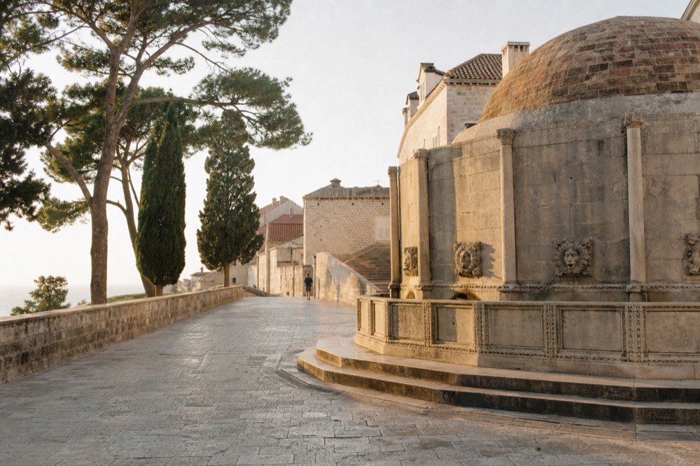 An old stone fountain lit by warm evening light with empty steps around it in a quiet square