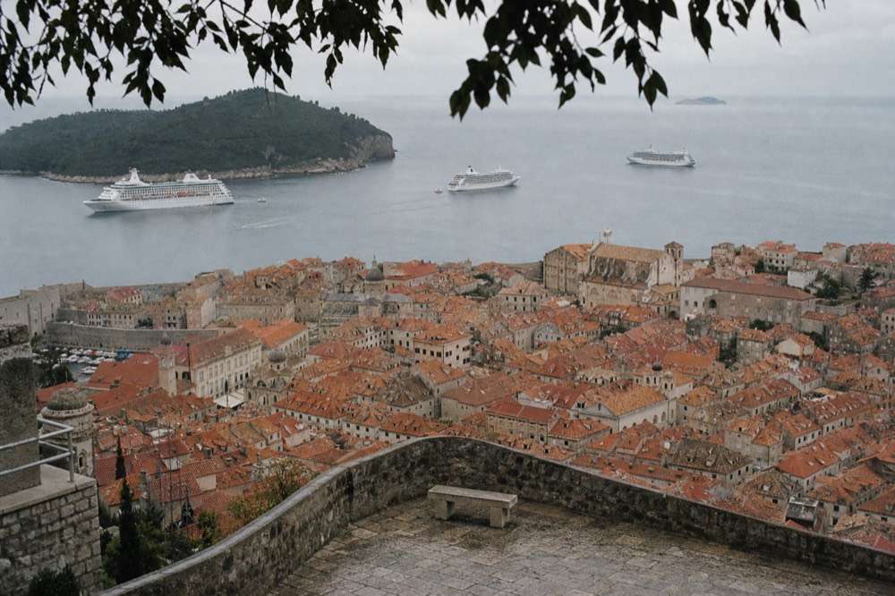An aerial view of Dubrovnik Old Town rooftops with cruise ships anchored in the bay beyond