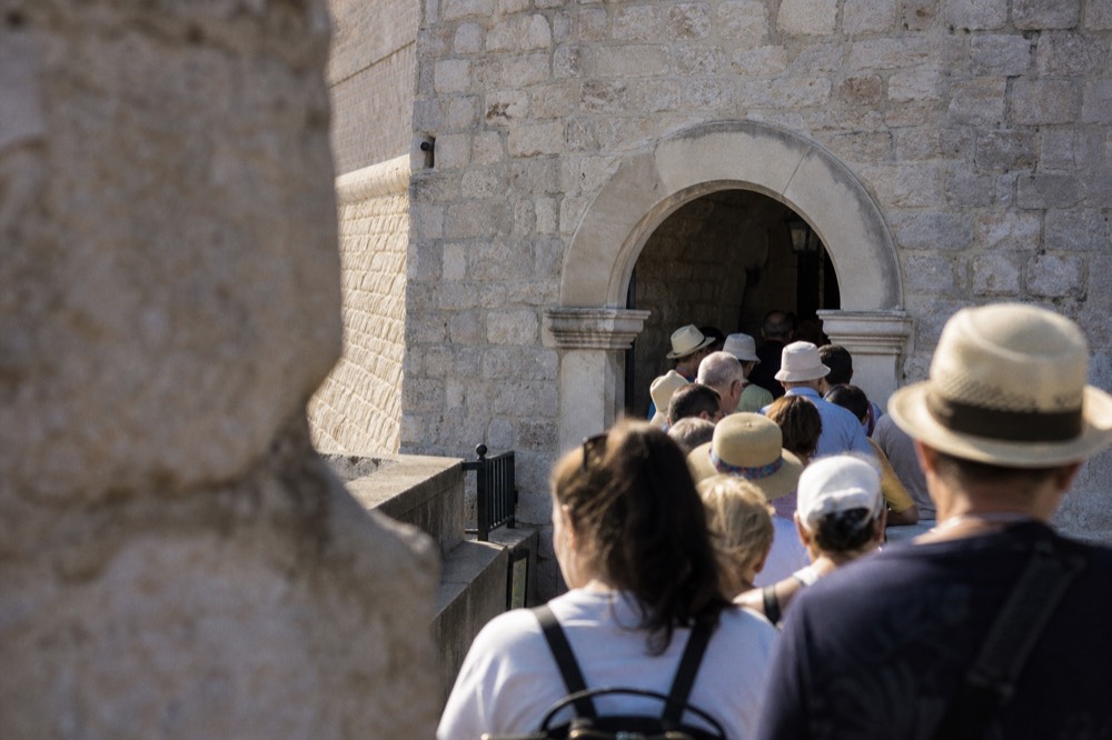 A queue of visitors waiting at a stone gate entrance to the Dubrovnik city walls