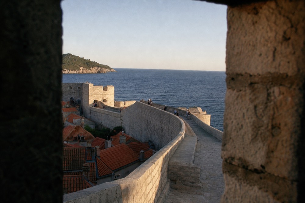 The stone city walls of Dubrovnik curving above red rooftops toward the blue Adriatic