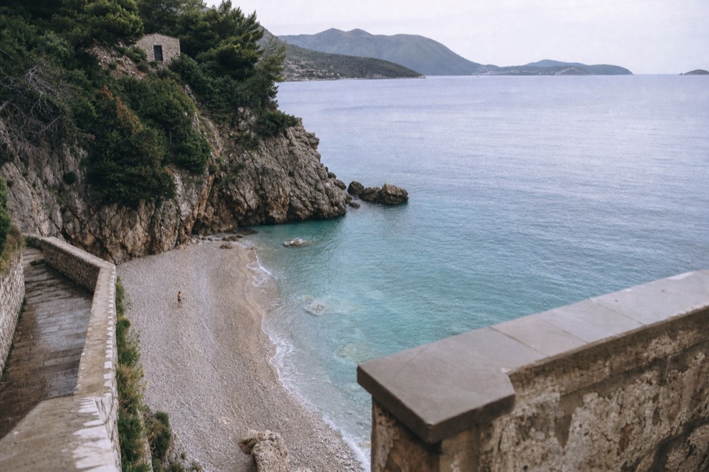A quiet pebble beach with clear turquoise water below cliffs near Dubrovnik