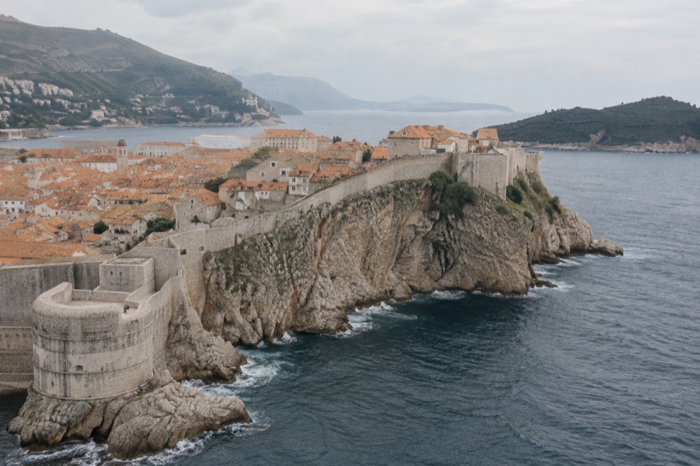 The Dubrovnik city walls seen from above curving along the coastline with the sea beyond