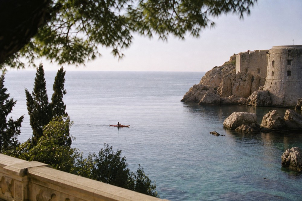 A sea kayak gliding over clear water toward rocky cliffs near Dubrovnik