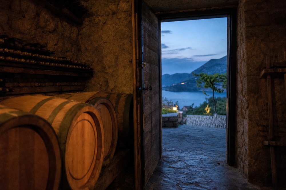 A wine cellar with oak barrels and bottles racked along stone walls